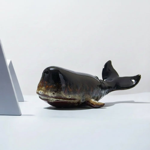 Black ceramic fish sculpture on a white surface with a plain background