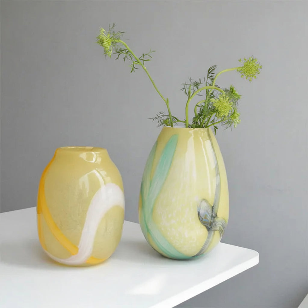 Two glass vases with marbled patterns and greenery on a gray background